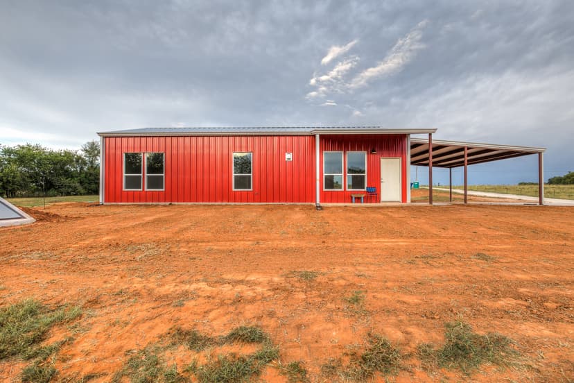 Red metal barndominium on a freshly graded red dirt pad on open Oklahoma acreage